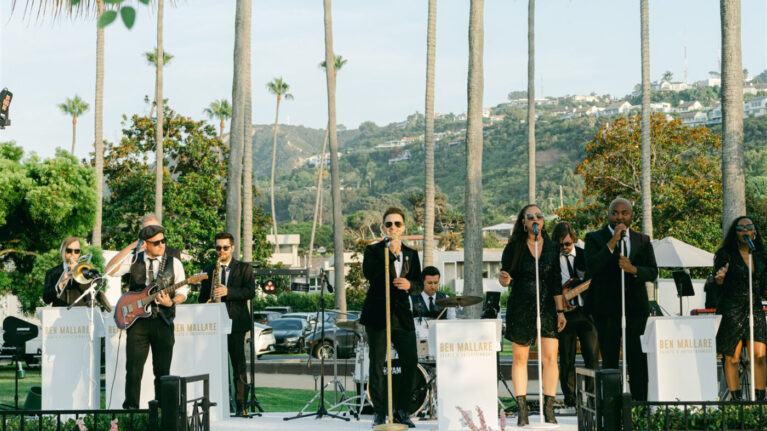 A vibrant live wedding band performance featuring a 20-piece ensemble, showcasing talented musicians and vocalists on stage, perfect for creating an unforgettable atmosphere at weddings. The image highlights Ben Mallare Events & Entertainment, renowned for delivering high-energy musical experiences that elevate wedding celebrations. Beautiful floral arrangements surround the stage, enhancing the festive ambiance for brides and grooms seeking exceptional live entertainment.