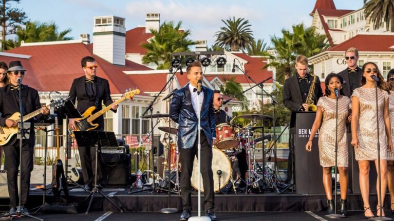 A 20-piece wedding band from Ben Mallare Events & Entertainment performing live on stage, featuring musicians and singers with instruments, set against a scenic outdoor venue backdrop.