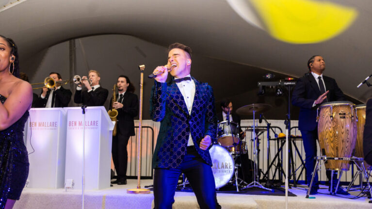 A 20-piece live wedding band from Ben Mallare Events & Entertainment performing on stage with a lead singer, saxophonist, and drummer, creating a vibrant atmosphere for a wedding celebration.