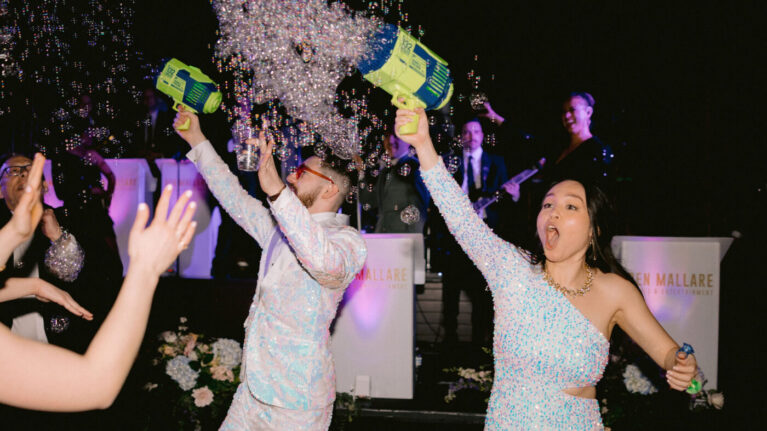 A lively wedding celebration featuring guests joyously dancing and spraying bubbles while a 20-piece wedding band performs on stage in the background. This vibrant scene captures the excitement and energy of live wedding entertainment, showcasing Ben Mallare Events & Entertainment's ability to create unforgettable moments at weddings. The musicians are seen engaging the audience, enhancing the festive atmosphere that makes live wedding bands a popular choice for couples.
