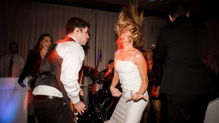 A bride and groom dance energetically in front of a live 20-piece wedding band from Ben Mallare Events & Entertainment, showcasing the vibrant atmosphere created by live wedding music.