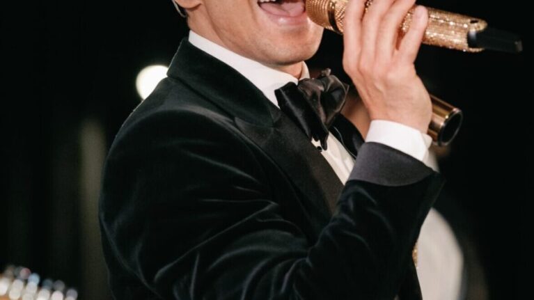 A charismatic male vocalist performs on stage, showcasing his talent as part of a dynamic 20-piece wedding band. The energy of the live wedding music creates an unforgettable atmosphere, ideal for making special memories at events like those organized by Ben Mallare Events & Entertainment.