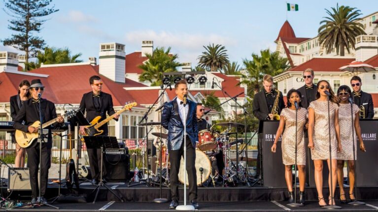 A vibrant 20-piece wedding band performs live on stage on the beach at Hotel Del Coronado, featuring talented musicians and singers, as they create an unforgettable atmosphere for a wedding celebration. The ensemble, part of Ben Mallare Events & Entertainment, showcases a mix of instruments including guitars, saxophones, and drums, set against a picturesque backdrop. This image highlights the energy and elegance of live wedding bands, perfect for couples looking to elevate their special day with exceptional music and entertainment.