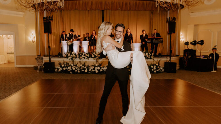 Couple enjoying their first dance at their Hotel Del Coronado wedding, with a vibrant 11-piece wedding band performing in the background. The scene captures the joy and elegance of live wedding music, highlighting Ben Mallare Events & Entertainment's exceptional talent in creating unforgettable wedding experiences. The beautifully decorated venue enhances the romantic atmosphere, making it an ideal setting for celebrating love through live performances.