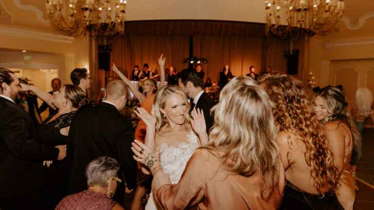 A lively wedding reception at Hotel Del Coronado featuring the Ben Mallare All-Stars Band performing on stage, with guests joyfully dancing and celebrating. The atmosphere is filled with excitement as the bride and her friends engage in the festivities, showcasing the vibrant energy that live music brings to special events. Ben Mallare Events & Entertainment provides exceptional live entertainment, ensuring unforgettable moments for couples and their guests.