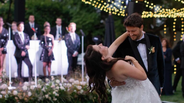 A bride and groom share a romantic dance under twinkling lights with a live 20-piece wedding band from Ben Mallare Events & Entertainment performing in the background.