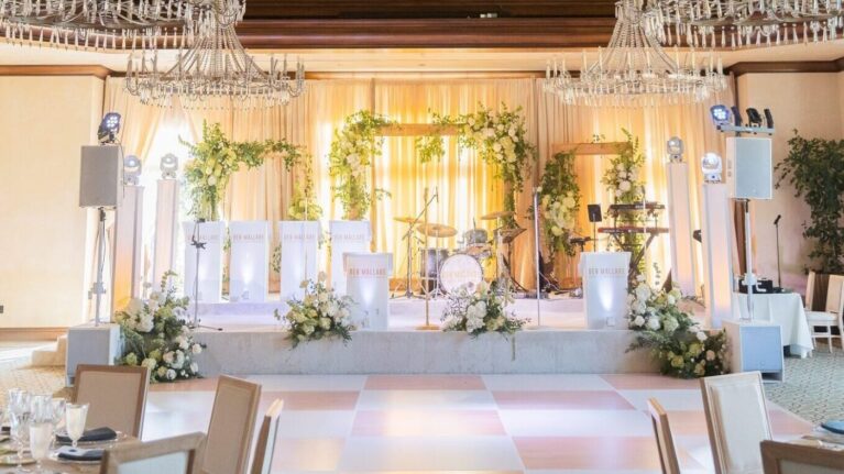 Elegant wedding reception setup featuring a stage prepared for a live wedding band performance, showcasing a 20-piece ensemble with instruments like drums and keyboards. The beautifully decorated venue by Ben Mallare Events & Entertainment includes floral arrangements and a polished dance floor, creating an inviting atmosphere for guests to enjoy unforgettable live music during the celebration. Ideal for couples seeking a memorable entertainment experience at their wedding.