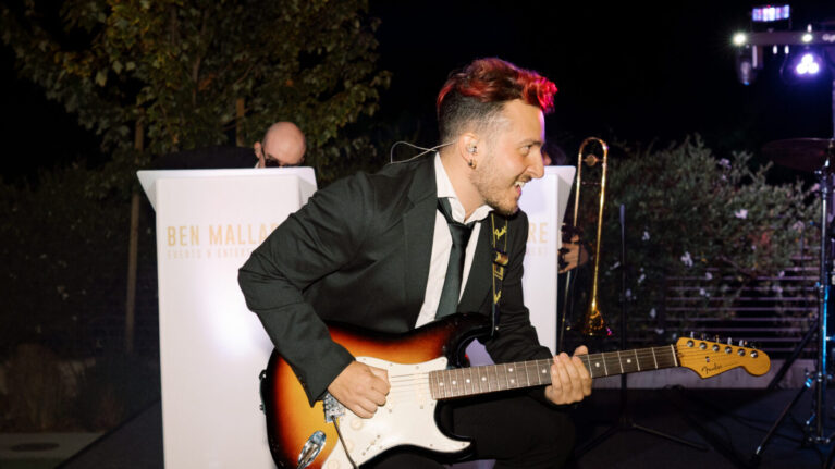 Guitarist performing energetically on stage with a live wedding band from Ben Mallare Events & Entertainment, showcasing a vibrant and engaging musical experience for wedding receptions.