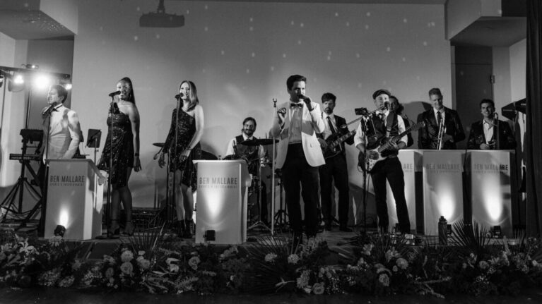 A 20-piece wedding band from Ben Mallare Events & Entertainment performing live on stage with vocalists and musicians playing instruments, creating an energetic atmosphere for a wedding celebration.
