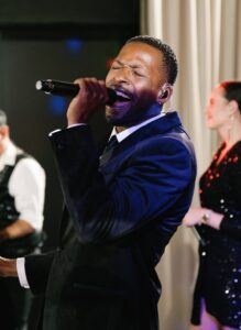 A dynamic live performance by a talented vocalist in a stylish suit, accompanied by musicians in the background, showcases the vibrant atmosphere created by a 20-piece wedding band from Ben Mallare Events & Entertainment. This live wedding band creates unforgettable moments with their engaging music and energetic stage presence, perfect for transforming any wedding celebration into a memorable experience.
