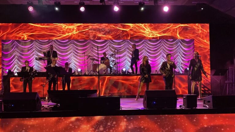 A vibrant 20-piece wedding band from Ben Mallare Events & Entertainment performing live on stage, featuring musicians and singers under dynamic lighting, perfect for live wedding entertainment. A vibrant 20-piece wedding band from Ben Mallare Events & Entertainment performing live on stage, featuring musicians and singers under dynamic lighting, perfect for live wedding entertainment.