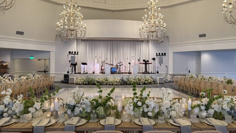 Elegant wedding reception setup at the Hotel Del Coronado ballroom, featuring a beautifully decorated stage for a live wedding band performance by Ben Mallare Events & Entertainment. The image showcases a 20-piece wedding band setup, with instruments ready for a memorable celebration, surrounded by stunning floral arrangements and an inviting dining area, perfect for creating unforgettable moments during the event.