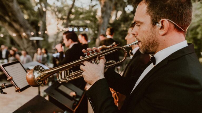 A 20-piece live wedding band performing on stage, featuring a trumpet player in the foreground, provided by Ben Mallare Events & Entertainment.