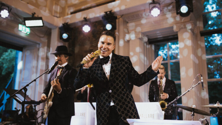 A vibrant 20-piece wedding band from Ben Mallare Events & Entertainment performing live, featuring a lead singer with a microphone, a guitarist, and a saxophonist on stage, creating an energetic atmosphere for a wedding celebration.