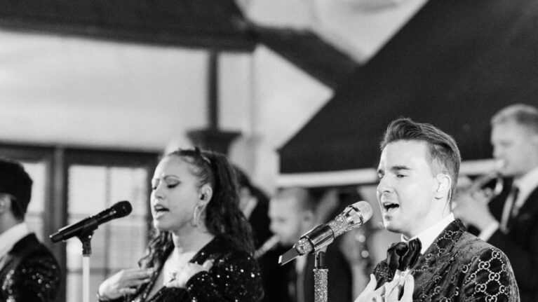 Black and white image of a 20-piece live wedding band performing on stage, featuring male and female vocalists, part of Ben Mallare Events & Entertainment, providing high-energy music for weddings and events.