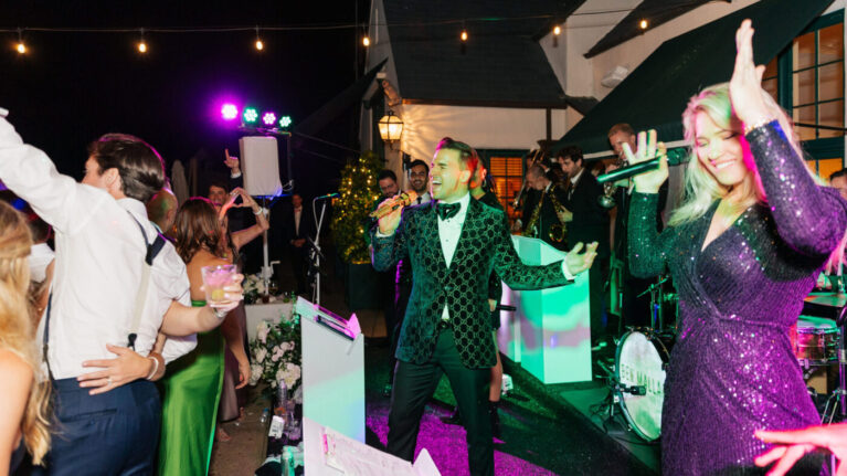 A vibrant 20-piece wedding band from Ben Mallare Events & Entertainment performing live at an elegant outdoor wedding reception, featuring a charismatic lead singer and talented musicians playing various instruments under colorful stage lights.