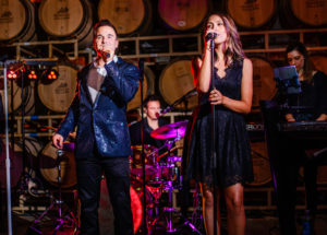 Live wedding band from Ben Mallare Events & Entertainment performing on stage, featuring a male and female singer with a drummer in the background.