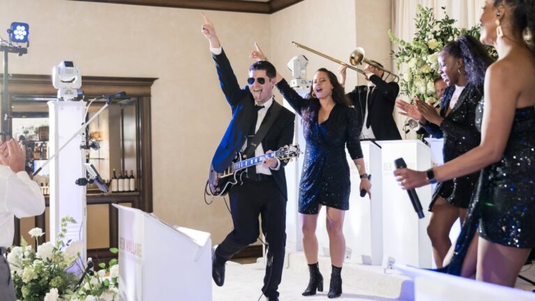 A lively performance by a 20-piece wedding band at a wedding event, featuring musicians on stage, including a guitarist and vocalists in glamorous attire, creating an energetic atmosphere. This image showcases the vibrant entertainment provided by Ben Mallare Events & Entertainment, perfect for making any wedding unforgettable with live music.