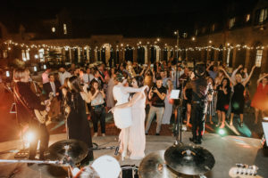 A lively 20-piece wedding band from Ben Mallare Events & Entertainment performing on stage, entertaining a large crowd of wedding guests dancing under string lights.