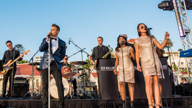 A dynamic live performance at a Hotel Del Coronado wedding, featuring an 11-piece wedding band from Ben Mallare Events & Entertainment, showcasing talented musicians and vocalists on stage. The image captures the energy of the event, highlighting the band's stylish outfits and engaging presence, perfect for creating an unforgettable atmosphere at weddings. Live wedding bands like this one add a unique touch to celebrations, ensuring memorable moments for couples and their guests.