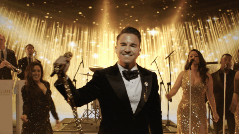 Lead singer of a 20-piece wedding band performing on stage with golden backdrop, part of Ben Mallare Events & Entertainment.