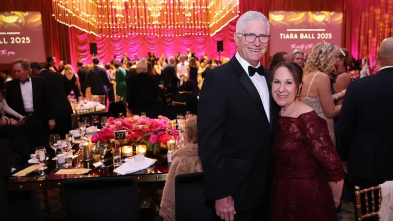 A couple smiles at the Tiara Ball 2025, surrounded by elegantly dressed guests enjoying the vibrant atmosphere created by live wedding bands. The event showcases a lively 20-piece wedding band performing on stage, enhancing the celebratory mood. Colorful floral centerpieces and candlelight adorn the tables, highlighting the luxurious ambiance crafted by Ben Mallare Events & Entertainment for memorable celebrations.